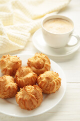 Homemade profiteroles with cream on plate with cup of coffee on white background. Fresh baked golden profiterole. Vertical photo