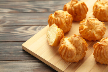 Homemade profiteroles with cream on plate on brown background. Fresh baked golden profiterole.