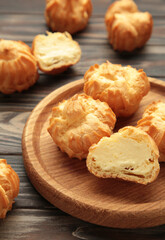 Homemade profiteroles with cream on wooden plate on brown background. Fresh baked golden profiterole. Vertical photo