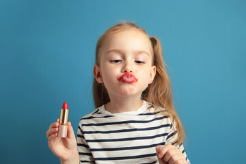 Happy little girl puts lipstick on her lips on blue background. Little trendy. little girl applying makeup