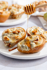 Baked pears with blue cheese, walnuts and honey on white plate and light background