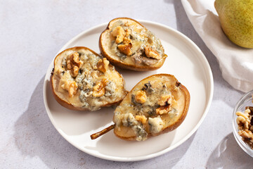 Baked pears with blue cheese, walnuts and honey on white plate and light background