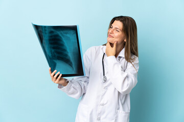 Young doctor woman holding radiography over isolated background looking to the side and smiling