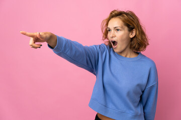 Young Georgian woman isolated on pink background pointing away