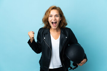 Georgian girl holding a motorcycle helmet isolated on blue background celebrating a victory in...