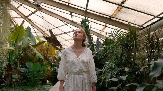 Beautiful young happy woman walking in spring park, tropical botanical garden among palm leaves, trees