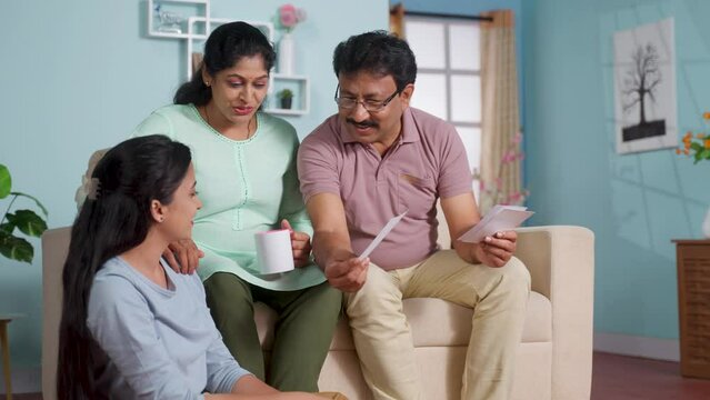 Happy indian father with mother showing marriage proposal photos to shying daughter at home - concept of family responsibility, arranged marriage and Future Plans