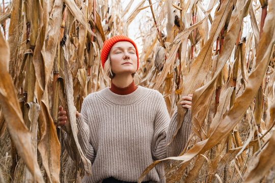 Relaxed and confident woman with eyes closed on background of dried corn field in autumn.