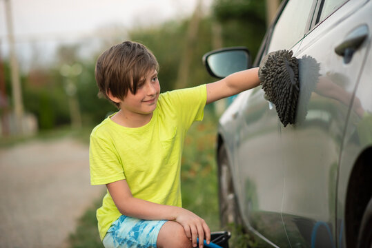 A 10-year-old boy helps his parents wash or dry the car. the child washes or wipes the car with a washcloth-mitten.
