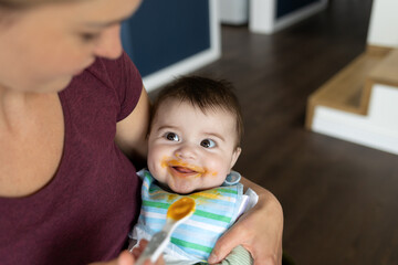 Happy baby boy eating first food pumpkin from spoon with mom at home