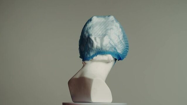 Closeup shot. Ancient marble bust statue of roman era woman in bouffant and face mask spins on a platform. Isolated on grey background.
