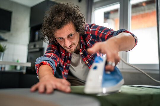 one man ironing clothes at home hold iron household chores concept - Powered by Adobe