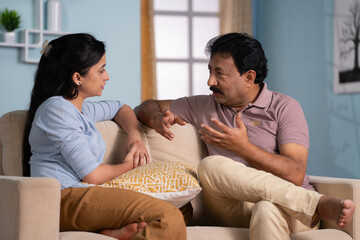 Indian father advising or guiding to young daughter while sitting on sofa at home - concept of...