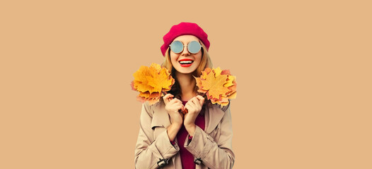Autumn color style outfit, portrait of beautiful smiling young woman with yellow maple leaves wearing red french beret hat, jacket on brown studio background