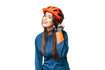 Young cyclist woman over isolated chroma key background listening to something by putting hand on the ear