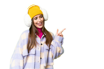 Young woman wearing winter muffs over isolated chroma key background pointing finger to the side and presenting a product