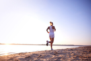 Rear view full length portrait of young healthy woman, training, running at beach near sea on sunrise. Morning fitness exercise in motion.