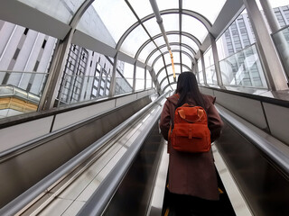 A young female tourist is standing on an escalator to get out of the subway station onto the street.