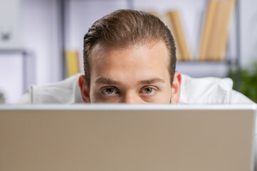 Lebanese confident businessman hiding behind laptop computer, looking at camera, spying his...