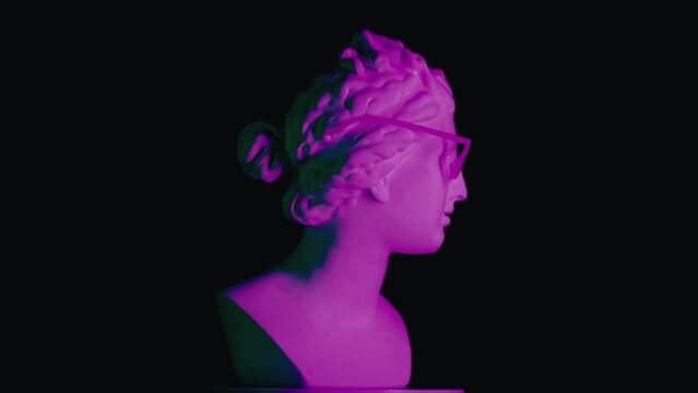 Closeup shot. Ancient marble bust statue of roman era woman in glasses spinning round on a platform in purple light. Isolated on black background.