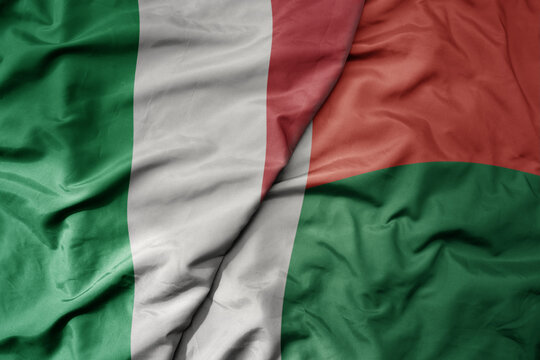 big waving national colorful flag of italy and national flag of madagascar .