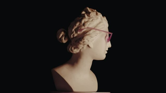 Closeup shot. Ancient marble bust statue of roman era woman in pink glasses spinning round on a platform. Isolated on black background.