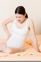 Pregnant Lady Having Massaging Lower belly Sitting On Sofa Indoor. Pregnancy Problems Concept. Maternity healthcare