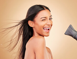 Wink, hair and portrait of happy woman with hairdryer for beauty isolated in a studio brown...