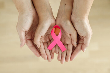 Mother and daughter's hands holding a pink ribbon, top view, Breast cancer awareness 