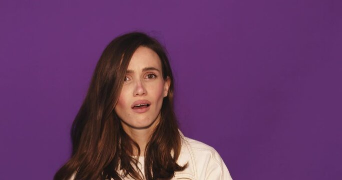 You lose! Brunette young woman wear white jacket making loser gesture, L sign on forehead, teasing and accusing for defeat, expressing disrespect. Indoor studio shot isolated on purple background.