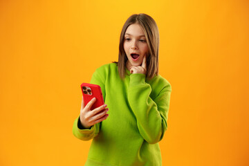 Surprised teen girl using mobile phone against yellow background