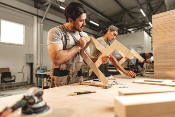 Two young men carpenters making furniture in warehouse of wood factory