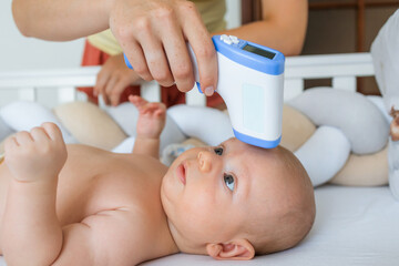 Unrecognizable woman measuring temperature to a cheerful baby. Health check