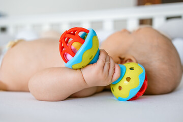 baby is lying at home on the bed , holding a rattle toy