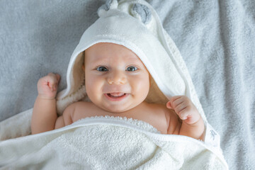 Fototapeta na wymiar Cute infant baby in white hood bathrobe on changing table after bath.