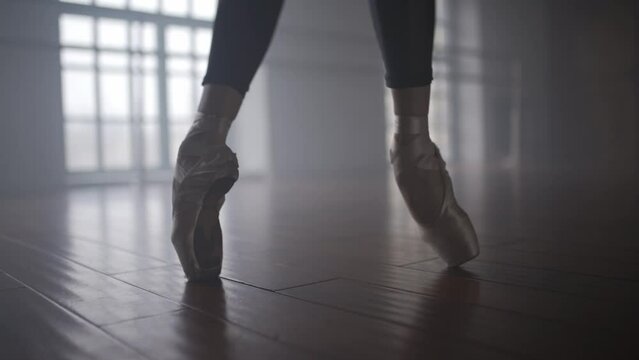 Ballerina in pointe shoes dancing on the floor. Dancer's legs close up. Dance ballet training in the hall