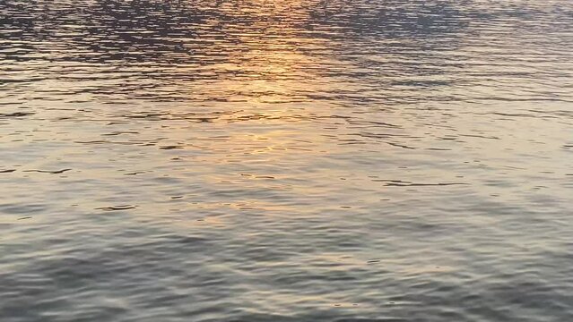 Shimmering reflection of orange and yellow sunset light on water, light sparkles on water waves, natural scenery, calm mesmerizing scene, sunlight