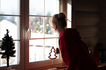 A girl in a red hoodie stands at the window and watches the winter view