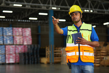 factory worker working on tablet and pointing to something in the warehouse storage