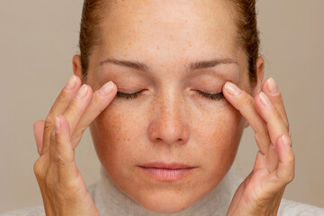 Middle aged caucasian woman of 40s with closed eyes holding fingers on eyelids to show eyes aging 