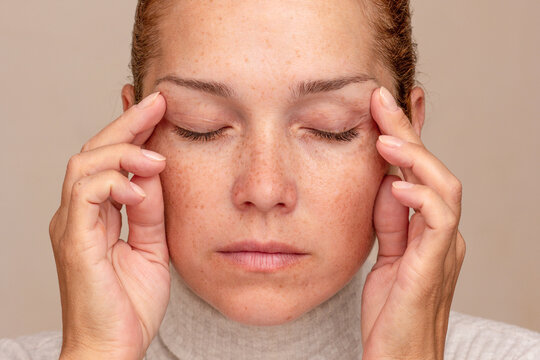 Middle aged caucasian woman of 40s with closed eyes holding fingers on temples to show migraine 