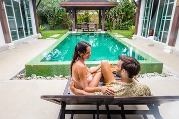 Fototapeten Couple of lovers in a beautiful tropical villa with swimming pool - Handsome man and pretty young woman having fun and relaxing in the home garden during summer vacation © oneinchpunch