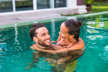 Fototapeta premium Couple of lovers in a beautiful tropical villa with swimming pool - Handsome man and pretty young woman having fun and relaxing in the home garden during summer vacation