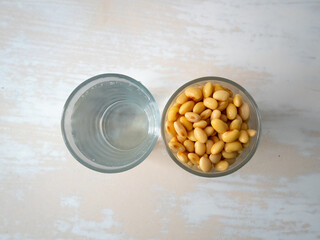 Soaked Soybeans in a Glass next to a Glass of Water on a White Table