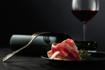 Prosciutto with rosemary and red wine on a black background.