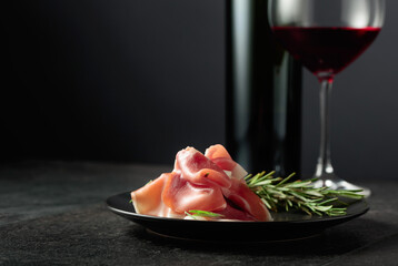 Prosciutto with rosemary and red wine on a black background.