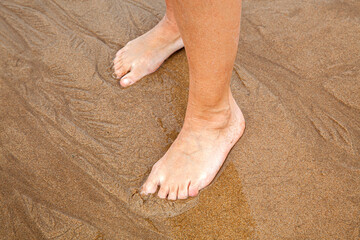 pies de mujer  descalza sobre la arena al borde del mar en la playa 