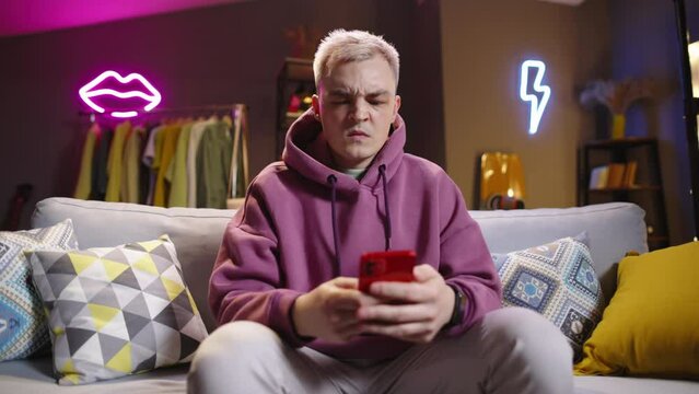Man scrolls through feed on social networks, coming across ugly content and provocative posts. Disgruntled man with frustrated expression. Abundance of negative disgusting content, evil toxic comments
