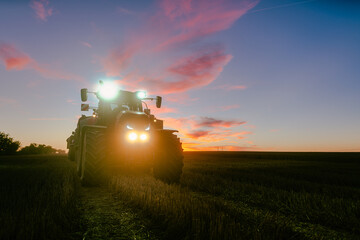 End of a harvest day on a grain field in summer with tractor with the last light during dusk