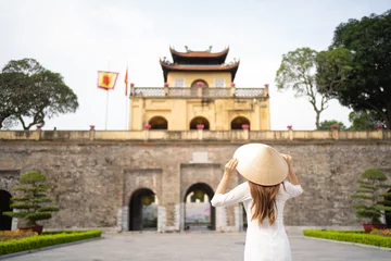 Fotobehang Portrait of Asian Vietnamese woman with Vietnam dress and straw hat travel at Imperial Citadel of Thang Long, Tourist attraction landmark in urban city town of Hanoi, Vietnam. People lifestyle. © tampatra
